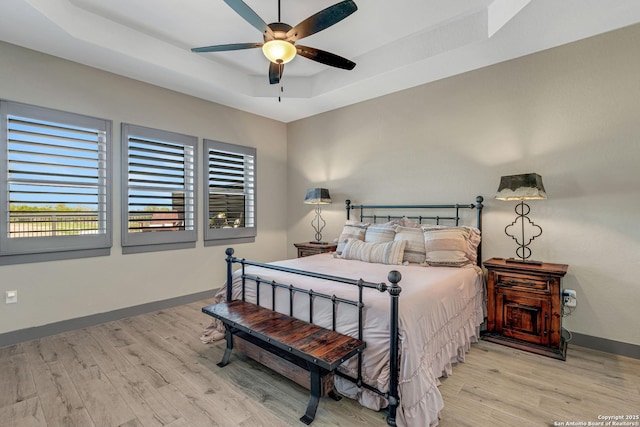 bedroom featuring ceiling fan, baseboards, a raised ceiling, and wood finished floors