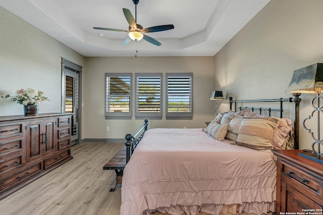 bedroom featuring a tray ceiling, baseboards, light wood-style flooring, and a ceiling fan