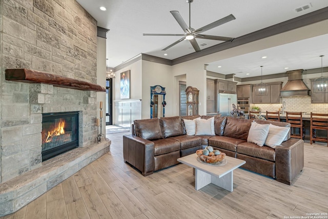 living area with visible vents, a fireplace, ceiling fan, ornamental molding, and light wood-type flooring