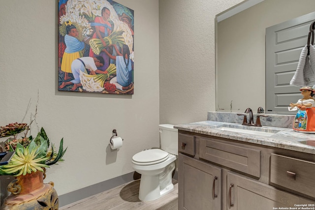 bathroom with vanity, toilet, wood finished floors, and baseboards