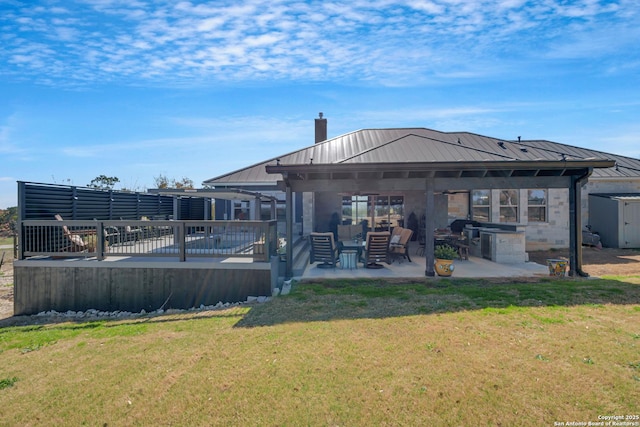 back of house with metal roof, a patio, a lawn, and a chimney