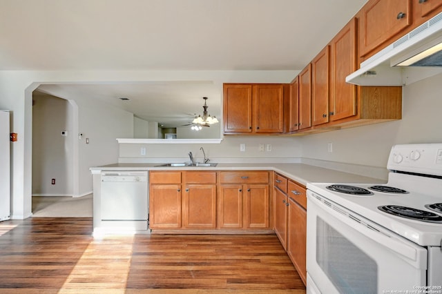 kitchen featuring light wood-type flooring, under cabinet range hood, a sink, white appliances, and light countertops