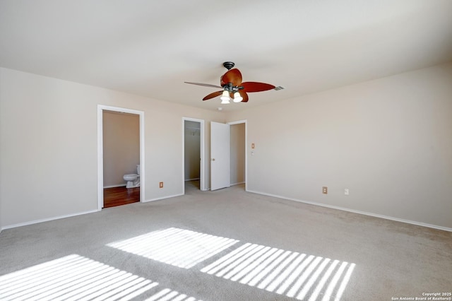 unfurnished bedroom with baseboards, ceiling fan, a spacious closet, light carpet, and connected bathroom