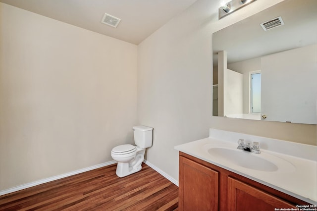 half bath with vanity, toilet, wood finished floors, and visible vents