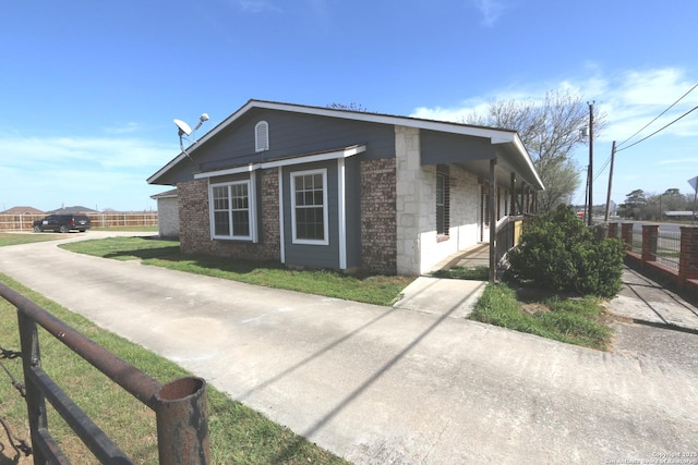 view of side of property with stone siding, a lawn, and fence