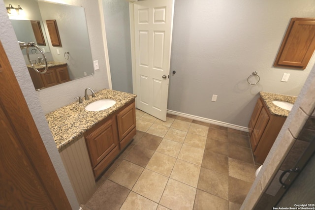 full bathroom with tile patterned flooring, two vanities, baseboards, and a sink