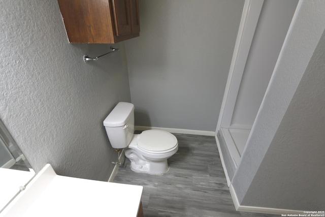 bathroom with baseboards, toilet, wood finished floors, and a textured wall