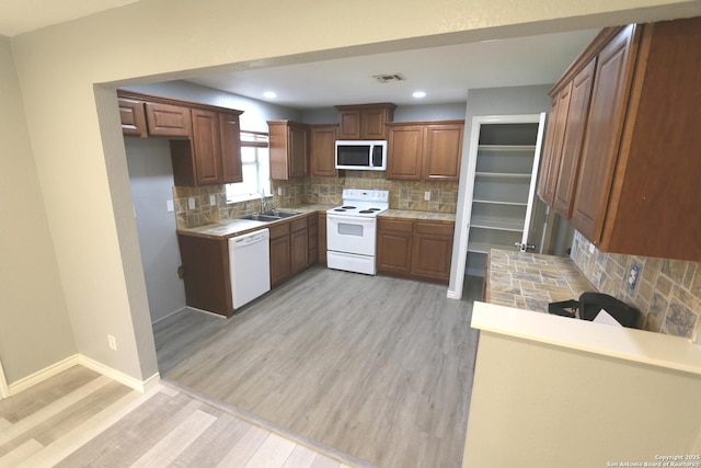 kitchen with visible vents, a sink, white appliances, light wood-style floors, and baseboards