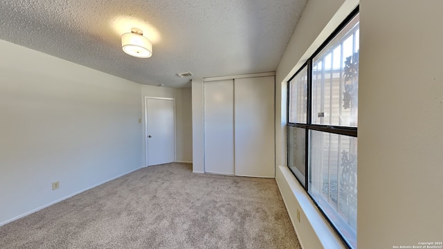 unfurnished bedroom featuring visible vents, a textured ceiling, a closet, and carpet flooring