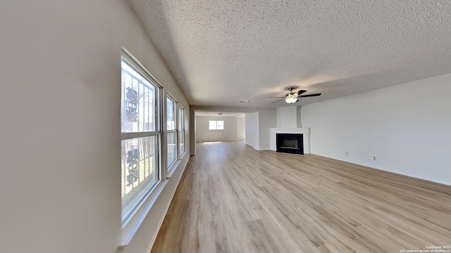 unfurnished living room featuring a fireplace, a textured ceiling, light wood-style flooring, and a ceiling fan