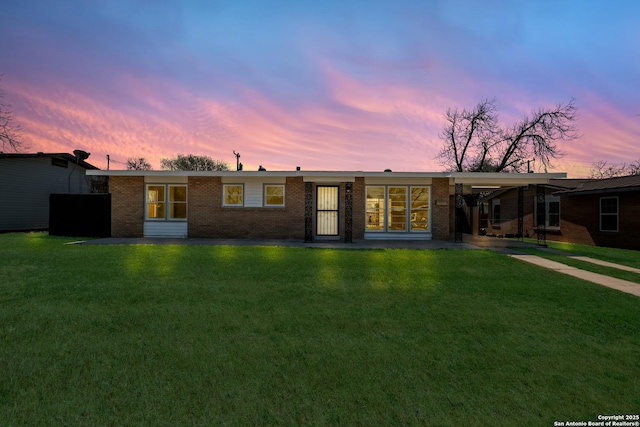 single story home featuring driveway, an attached carport, brick siding, and a lawn