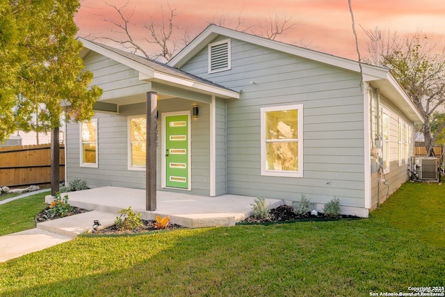 view of front of house with central air condition unit, a front lawn, and fence