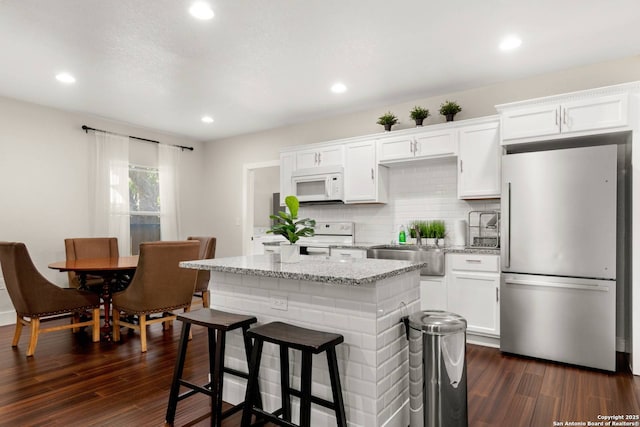 kitchen with white appliances, dark wood finished floors, a center island, and white cabinets