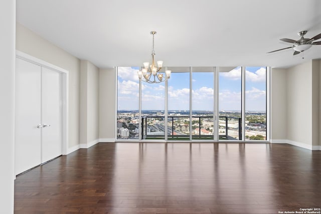 empty room with a city view, ceiling fan with notable chandelier, expansive windows, wood finished floors, and baseboards