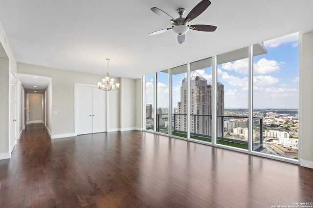 empty room featuring a city view, ceiling fan with notable chandelier, expansive windows, wood finished floors, and baseboards