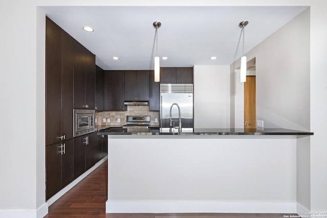 kitchen with under cabinet range hood, built in appliances, dark brown cabinets, and dark wood-style flooring