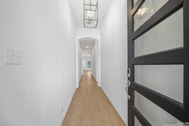 hallway featuring arched walkways, baseboards, and light wood-style floors