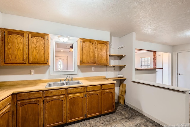 kitchen with brown cabinetry, open shelves, a sink, light countertops, and a textured ceiling