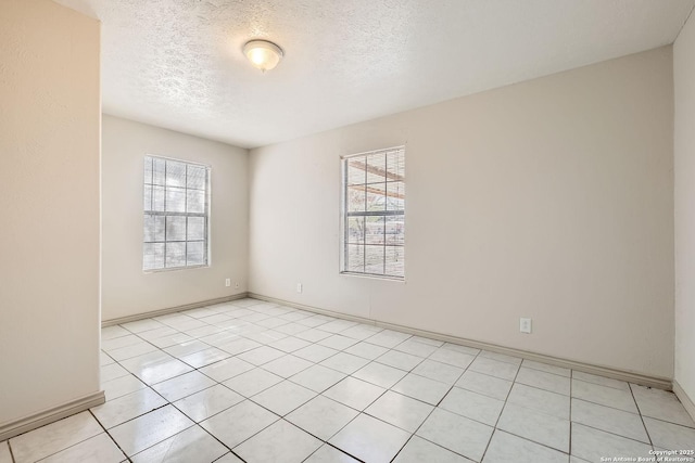 empty room with light tile patterned floors, a healthy amount of sunlight, a textured ceiling, and baseboards