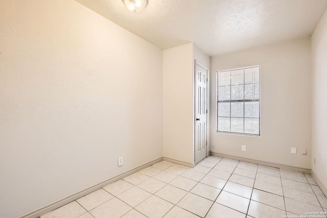 empty room featuring light tile patterned floors, a textured ceiling, and baseboards