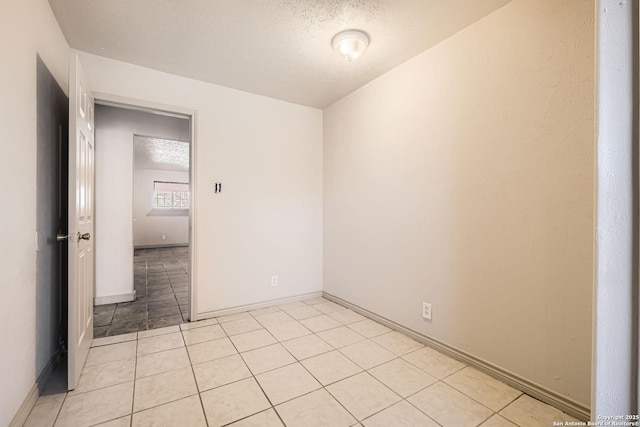 spare room with light tile patterned floors, baseboards, and a textured ceiling