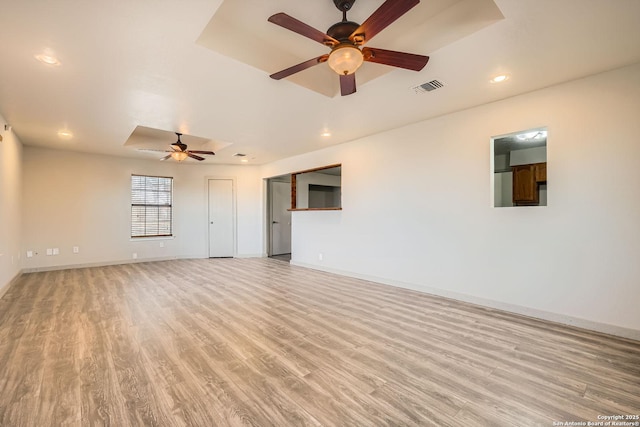 unfurnished room featuring visible vents, a tray ceiling, light wood-style floors, baseboards, and ceiling fan