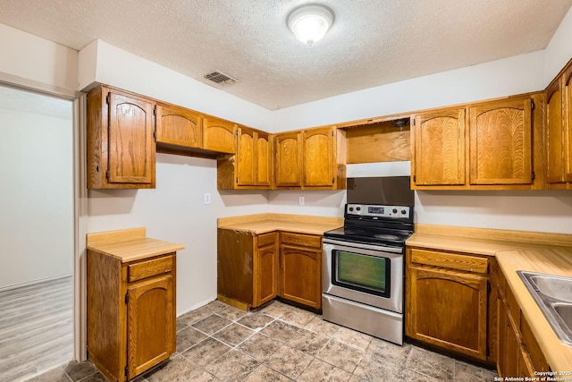 kitchen with visible vents, brown cabinets, stainless steel range with electric stovetop, and light countertops