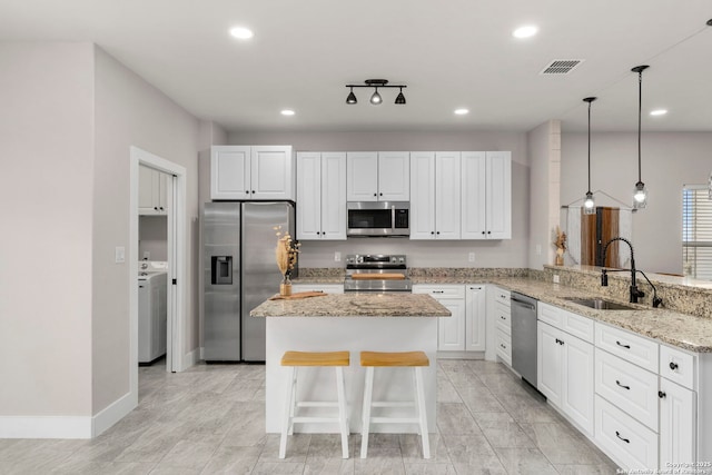 kitchen with visible vents, light stone counters, a peninsula, stainless steel appliances, and a sink