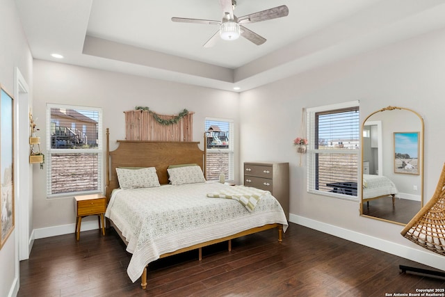 bedroom with a ceiling fan, a tray ceiling, wood finished floors, and baseboards