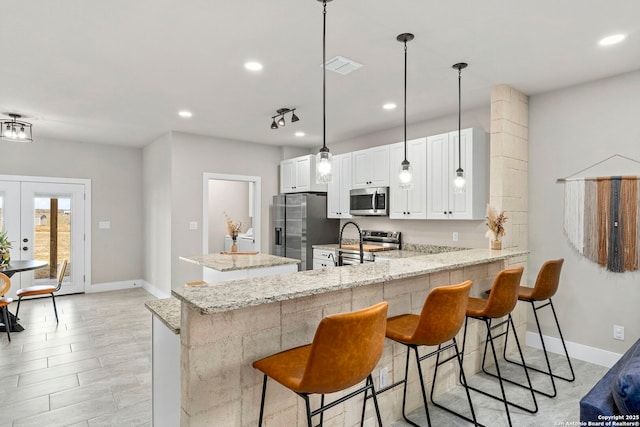 kitchen with a peninsula, light stone counters, visible vents, and appliances with stainless steel finishes