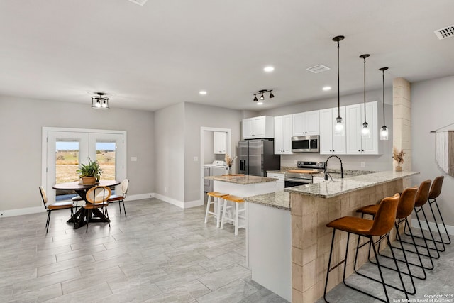 kitchen with a kitchen bar, visible vents, appliances with stainless steel finishes, a peninsula, and light stone countertops