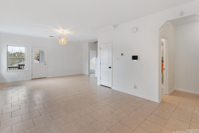 spare room featuring arched walkways, light tile patterned floors, a notable chandelier, and baseboards