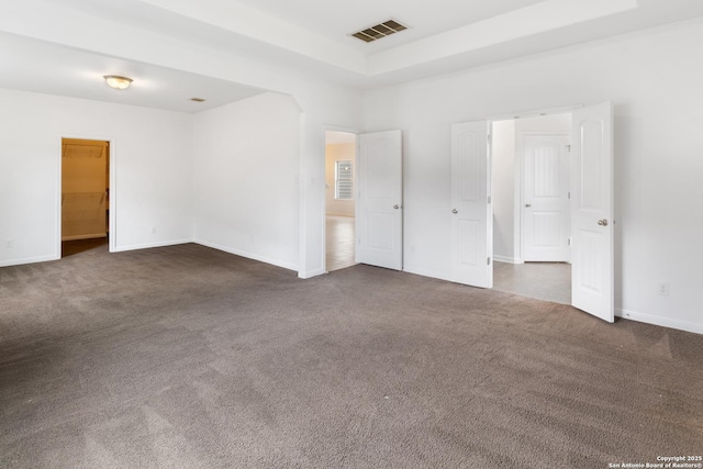 spare room featuring visible vents, a raised ceiling, baseboards, and dark carpet