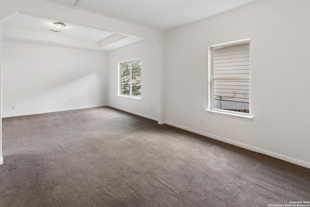 carpeted empty room with visible vents, a raised ceiling, and baseboards