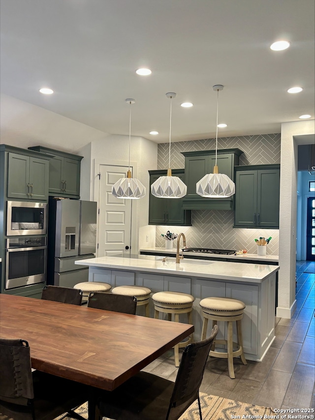 kitchen with an island with sink, decorative backsplash, appliances with stainless steel finishes, and light countertops