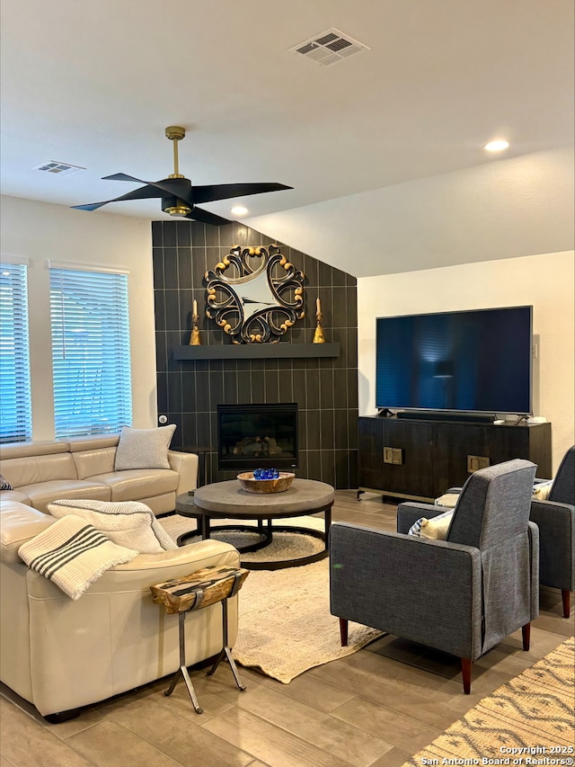 living area with vaulted ceiling, a ceiling fan, visible vents, and a tile fireplace