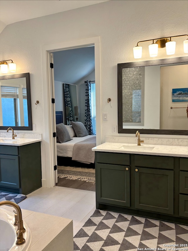 ensuite bathroom with ensuite bath, two vanities, vaulted ceiling, and a sink