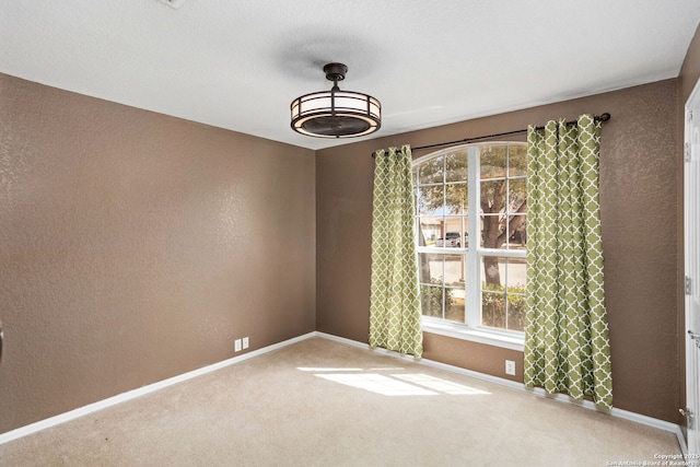 carpeted empty room featuring a textured wall and baseboards