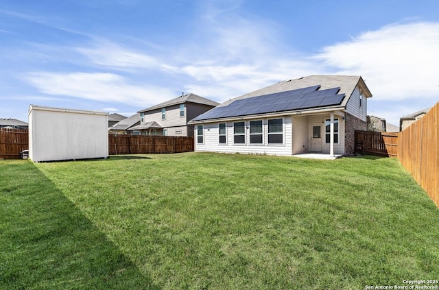 back of house with an outbuilding, a shed, solar panels, a fenced backyard, and a lawn