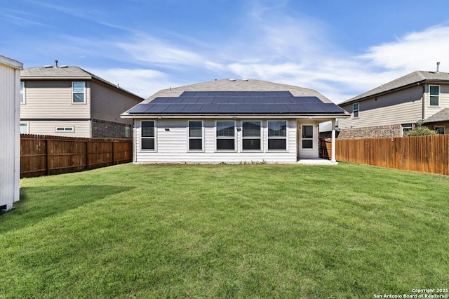 back of property featuring a lawn, solar panels, a fenced backyard, and a shingled roof