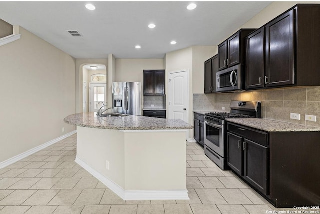 kitchen with light tile patterned floors, arched walkways, a sink, appliances with stainless steel finishes, and tasteful backsplash