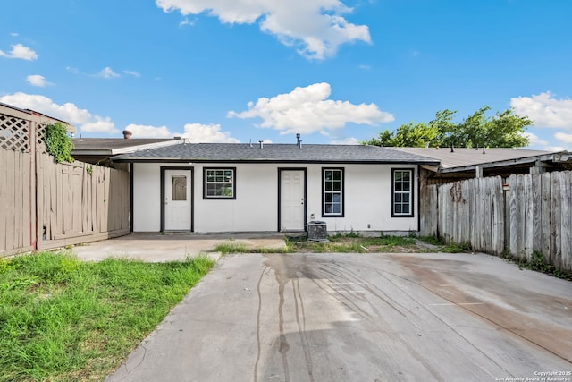 view of front of property with stucco siding, roof with shingles, central AC, and fence