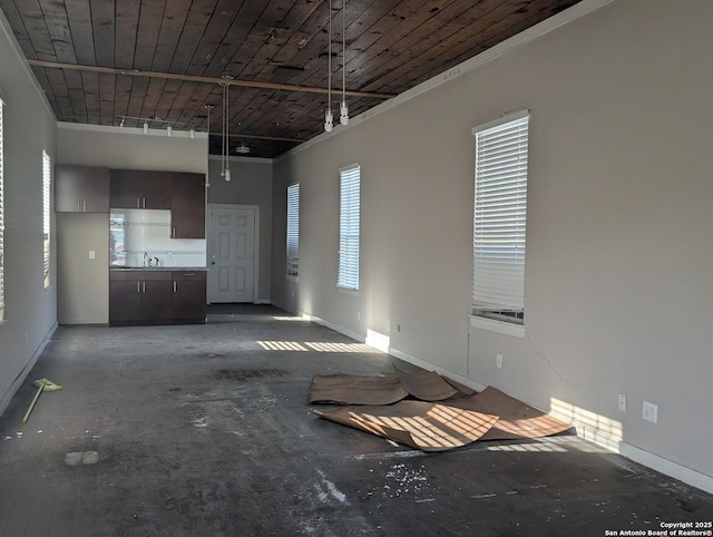 unfurnished living room featuring wooden ceiling, unfinished concrete floors, baseboards, and a sink