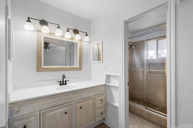 full bath with vanity, a textured ceiling, a shower stall, and tile patterned flooring