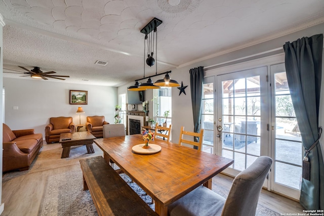 dining area featuring light wood finished floors, a tiled fireplace, french doors, a textured ceiling, and a ceiling fan