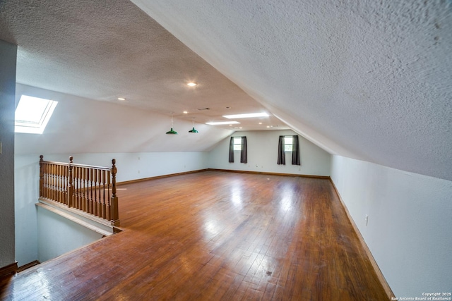 bonus room with baseboards, a textured ceiling, lofted ceiling with skylight, and hardwood / wood-style flooring