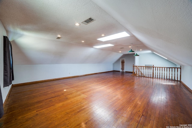 bonus room featuring lofted ceiling with skylight, visible vents, baseboards, and wood-type flooring