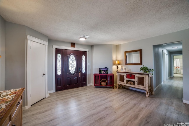 foyer with visible vents, a textured ceiling, baseboards, and light wood-style floors