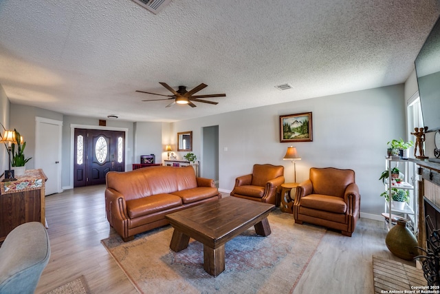 living area featuring visible vents, baseboards, ceiling fan, light wood-style floors, and a textured ceiling