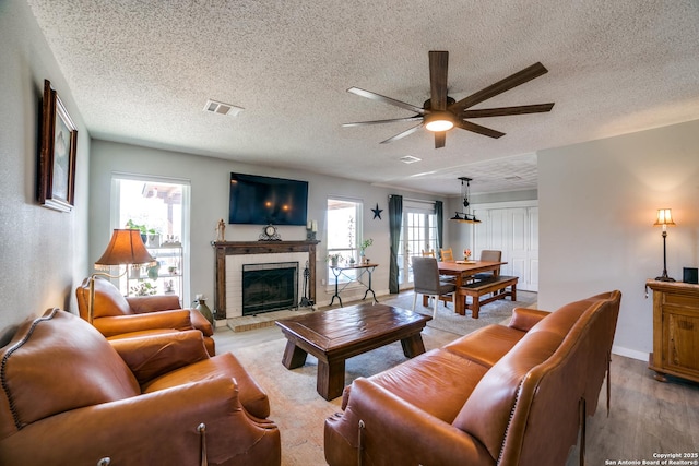 living room with baseboards, visible vents, light wood finished floors, ceiling fan, and a brick fireplace